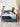 A couple making their bed with a Serta Antarctic mattress featuring a black and light blue border with All-Night Cooling Cooltex branding, on a grey upholstered bed frame