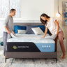 A couple making their bed with a Serta Antarctic mattress featuring a black and light blue border with All-Night Cooling Cooltex branding, on a grey upholstered bed frame