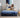 Mother reading a book while a child jumps happily on a Serta Classic Latex mattress with blue top and navy floral-pattern border on a beige upholstered bed frame