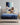 Mother reading a book while a child jumps happily on a Serta Classic Latex mattress with blue top and navy floral-pattern border on a beige upholstered bed frame