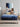 Mother reading a book while a child jumps happily on a Serta Classic Latex mattress with blue top and navy floral-pattern border on a beige upholstered bed frame