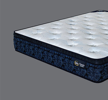 Angled view of Serta Classic Luxury mattress displaying white quilted bubble-tufted top and navy blue tie-dye floral-pattern border on a grey background