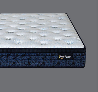 Corner angled view of Serta Classic Luxury mattress showcasing white bubble-tufted sleep surface and deep navy blue tie-dye floral-pattern side border