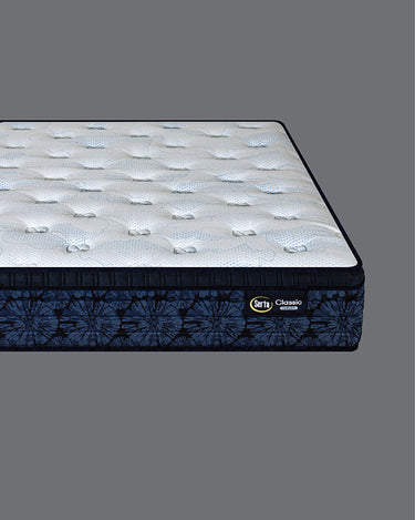 Corner angled view of Serta Classic Luxury mattress showcasing white bubble-tufted sleep surface and deep navy blue tie-dye floral-pattern side border