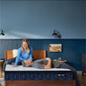Couple relaxing on a Serta Classic Luxury mattress with white tufted top and navy floral-pattern border on a wooden bed frame in a blue-walled bedroom