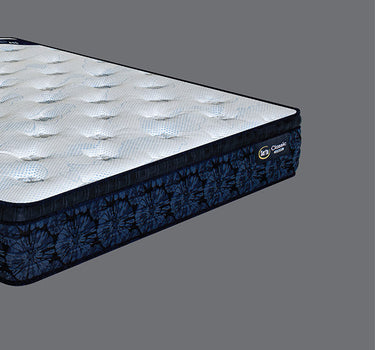 Low side-angle view of Serta Classic Luxury mattress highlighting the white tufted sleep surface and bold navy blue tie-dye floral side border with brand label