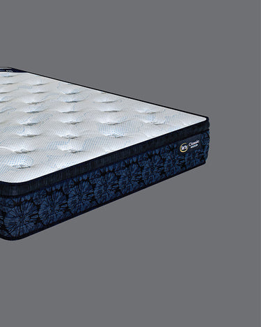 Low side-angle view of Serta Classic Luxury mattress highlighting the white tufted sleep surface and bold navy blue tie-dye floral side border with brand label