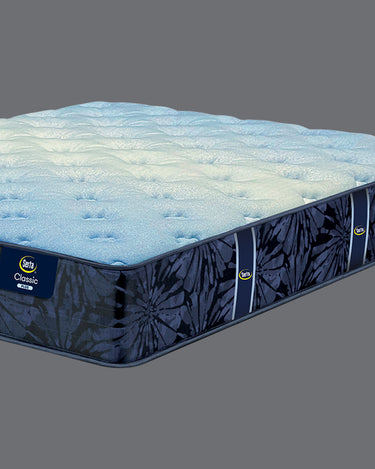 Close-up angled view of Serta Classic Plus mattress highlighting the plush light blue tufted top layer and bold navy blue floral-patterned side border with brand label