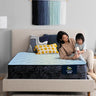 Mother and child sitting together on a Serta Classic Plus mattress with light blue quilted top on a beige upholstered bed frame in a cozy bedroom