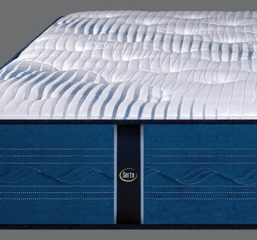 Close-up corner view of the Serta iLatex mattress highlighting the wave-quilted navy blue border with a Serta logo badge and thick pillow top