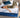 A woman relaxing on a Serta iLatex mattress with a white tufted top and navy blue quilted border, placed on a grey upholstered bed frame