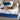 A woman relaxing on a Serta iLatex mattress with a white tufted top and navy blue quilted border, placed on a grey upholstered bed frame