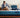 A couple relaxing on a Serta iPedic mattress with blue quilted sides, set on a wooden bed frame in a stylish bedroom