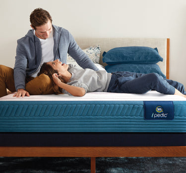 A couple relaxing on a Serta iPedic mattress with blue quilted sides, set on a wooden bed frame in a stylish bedroom