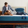 A couple relaxing on a Serta iPedic mattress with blue quilted sides, set on a wooden bed frame in a stylish bedroom
