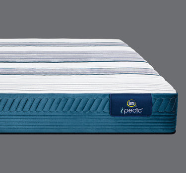Side profile view of the Serta iPedic mattress showcasing its white striped top and deep blue quilted border on a grey background