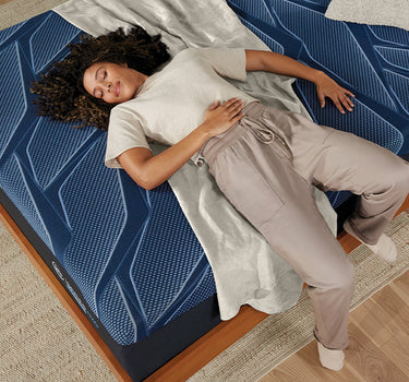 Overhead view of a woman sleeping comfortably on a Serta iSeries NXG Hybrid mattress with bold blue geometric pattern on a wooden platform bed