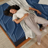 Overhead view of a woman sleeping comfortably on a Serta iSeries NXG Hybrid mattress with bold blue geometric pattern on a wooden platform bed