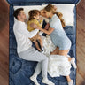 Overhead view of a family — parents and young child — sleeping together on a Serta Perfect Sleeper Hybrid mattress with navy blue floral radial-pattern fabric on a wooden bed frame