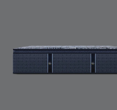 Side profile view of Serta Perfect Sleeper Hybrid mattress showing the pillow-top surface with grey floral-striped pattern and solid navy blue base border