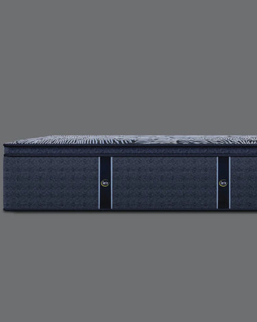 Side profile view of Serta Perfect Sleeper Hybrid mattress showing the pillow-top surface with grey floral-striped pattern and solid navy blue base border