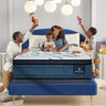 Happy family with two children playing on a Serta Perfect Sleeper mattress with white dash-quilted top and blue oval-patterned border on a navy upholstered bed frame