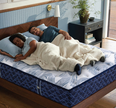 Couple sleeping comfortably on a Serta PerfectSpine mattress with blue wave-pattern fabric on a wooden bed frame in a modern bedroom